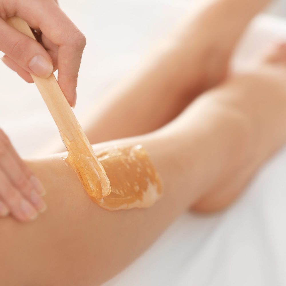 Beautician waxing female legs in spa center
